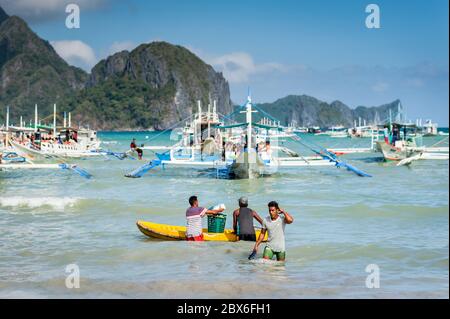 Les touristes et les mains de bateaux philippins locaux se sont emparés ou apportent des fournitures aux nombreux bateaux amarrés dans le surf attendant de visiter les îles et les plages. Banque D'Images