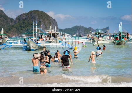 Les touristes à la plage de la ville d'El Nido se sont enlarés vers les nombreux bateaux à longue queue amarrés dans le surf attendant de visiter les îles et les plages. Banque D'Images