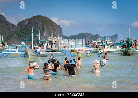 Les touristes à la plage de la ville d'El Nido se sont enlarés vers les nombreux bateaux à longue queue amarrés dans le surf attendant de visiter les îles et les plages. Banque D'Images