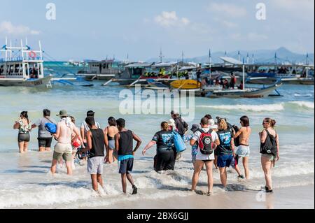 Les touristes à la plage de la ville d'El Nido se sont enlarés vers les nombreux bateaux à longue queue amarrés dans le surf attendant de visiter les îles et les plages. Banque D'Images