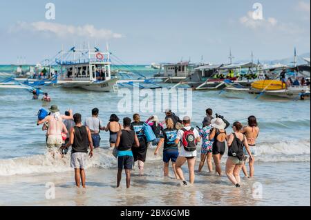 Les touristes à la plage de la ville d'El Nido se sont enlarés vers les nombreux bateaux à longue queue amarrés dans le surf attendant de visiter les îles et les plages. Banque D'Images