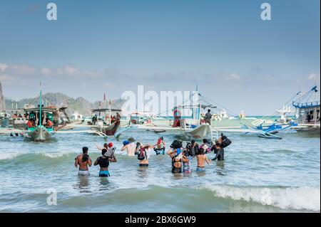 Les touristes à la plage de la ville d'El Nido se sont enlarés vers les nombreux bateaux à longue queue amarrés dans le surf attendant de visiter les îles et les plages. Banque D'Images