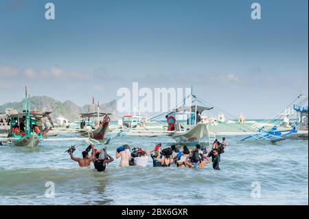 Les touristes à la plage de la ville d'El Nido se sont enlarés vers les nombreux bateaux à longue queue amarrés dans le surf attendant de visiter les îles et les plages. Banque D'Images