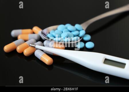 Pilules dans la cuillère et thermomètre numérique une table en verre foncé. Concept de médicaments antipyrétiques, antibiotiques, vitamines Banque D'Images