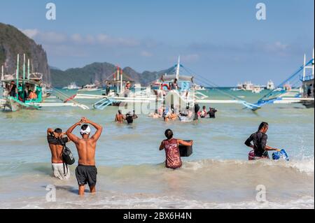 Les touristes et les mains de bateaux philippins locaux se sont emparés ou apportent des fournitures aux nombreux bateaux amarrés dans le surf attendant de visiter les îles et les plages. Banque D'Images