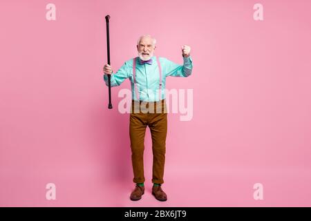 Photo pleine longueur d'un homme fou et âgé lever une canne à pied en colère grimace qui accuse les enfants voisins de comportement bruyant porter une chemise bretelles noeud cravate pantalon Banque D'Images
