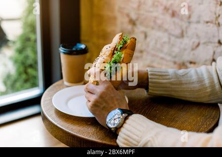 Gros plan image rognée de mains de sexe masculin tenant un croissant farci de laitue et de légumes frais. Concept café. Une alimentation saine. Déjeuner et petit déjeuner Banque D'Images