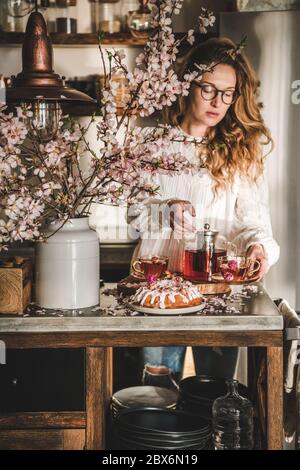 Jeune femme servant un gâteau maison et du thé dans la cuisine Banque D'Images