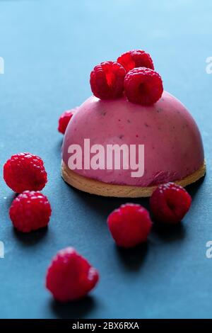 Tartelette à mousse aux framboises avec garniture de yogourt aux fraises décorée de framboises fraîches sur fond sombre minimaliste. Meilleur dessert aux baies d'été. Banque D'Images