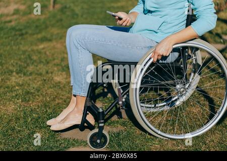 Une femme en fauteuil roulant avec un téléphone dans sa main marche dans la rue, sa main est proche, une méconnaissable Banque D'Images