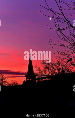 Ciel coloré au coucher du soleil avec des silhouettes d'une église et des arbres. Banque D'Images