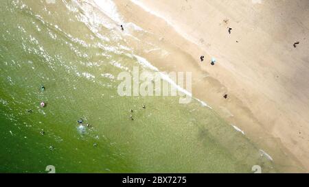 Vue aérienne sur la côte avec des personnes debout dans l'eau et sur la plage de sable blanc. Banque D'Images