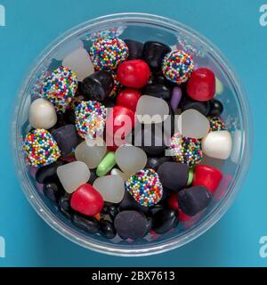 Assortiment de bonbons à la réglisse sur fond bleu dans un contenant en plastique transparent vu de dessus Banque D'Images