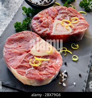 Tiges de veau Osso buco, crues, sur ardoise. Avec sel, poivre, persil et zeste de citron pour la gremolata. Banque D'Images