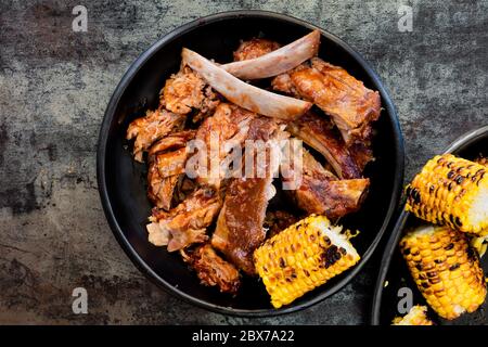 Griller les côtes de porc avec du maïs sucré grillé. Vue de dessus sur les plaques noires au-dessus de l'ardoise. Sauce collante. Banque D'Images