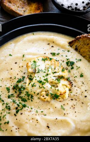 Soupe de chou-fleur rôtie dans un bol noir rustique, avec pain grillé au levain croustillant. Vue verticale. Banque D'Images