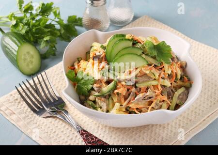 Salade avec coeurs de poulet, concombre, carottes et oignons dans un bol blanc sur fond bleu clair, format horizontal, gros plan Banque D'Images