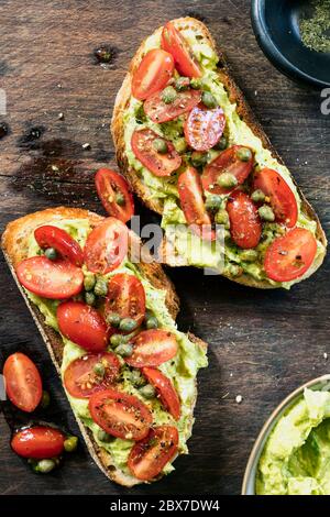 Toast à l'avocat avec tomates cerises et salsa au câpres. Pain au levain. Vue du dessus de l'ancienne planche. Banque D'Images