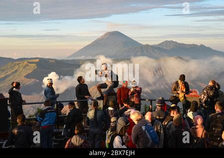 Les touristes prenant des selfies au point de vue sur le mont Penanjakan avec le volcan du mont Bromo en arrière-plan, une attraction touristique surpeuplée. Banque D'Images