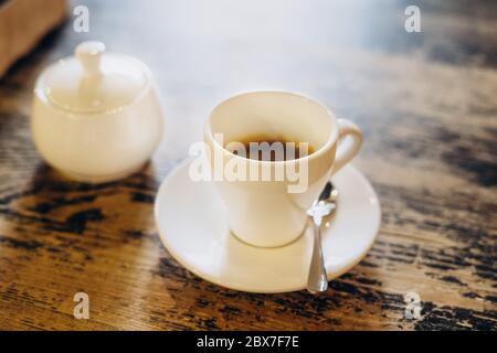 Café frais aromatique dans une tasse blanche. Americano avec un bol à sucre sur la table dans le café. Americano dans une petite tasse blanche Banque D'Images