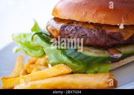 Grand hamburger juteux et délicieuses frites croquantes sur une assiette blanche. Gros plan extrême. Banque D'Images