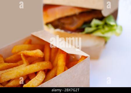 De délicieuses frites croquantes dans une boîte ouverte en carton durable. En face de hamburger juteux flou. Mise au point sélective et faible profondeur de Banque D'Images