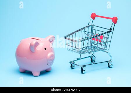 Banque de porc rose et chariot sur fond bleu. Le concept d'économie d'argent sur les achats dans le magasin Banque D'Images