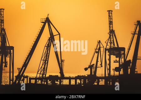 Silhouettes de grues de bateaux de mer sur un fond de coucher de soleil orange et chaud. Banque D'Images