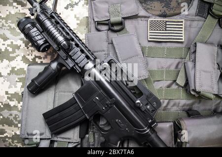 Vue de dessus photo d'un gilet militaire à l'épreuve des balles avec badge de drapeau américain et fusil sur un fond de tissu de camouflage. Banque D'Images