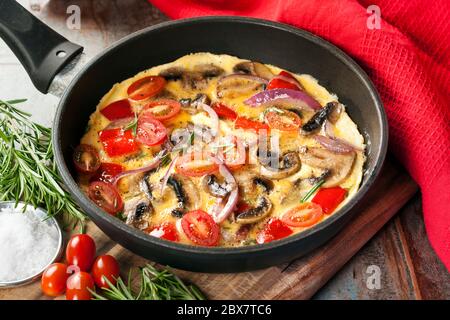 Omelette aux légumes cuite dans une poêle ou un poêlon. Champignons, poivrons, tomates prunes et oignons rouges. Banque D'Images