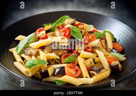 Pâtes aux aubergines, penne au piment et à la tomate, sur un plat de service noir. Garni de basilic. Banque D'Images