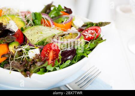 Salade dans un bol blanc. Légumes verts mélangés avec des olives noires, des tomates et beaucoup de légumes. Banque D'Images