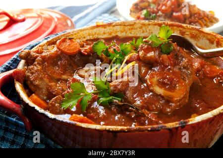 Délicieux jarrets de veau, cuits lentement avec des légumes, dans un crock-pot rouge. Buco osso traditionnel. Banque D'Images