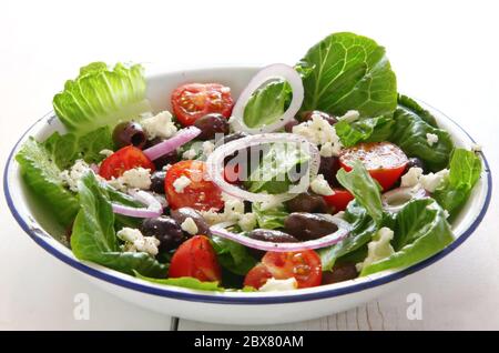 Salade grecque dans un ancien bol en émail. Laitue, tomates, oignon rouge, fromage de chèvre et olives noires. Banque D'Images