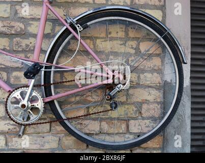 Roue de vélo rétro rose cassé accrochée sur un mur de briques jaunes Banque D'Images