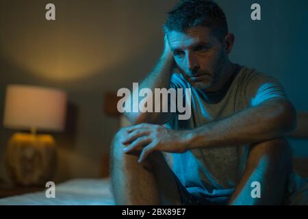 portrait dramatique dans l'obscurité d'un homme déprimé et inquiet sur le lit souffrant de la crise de dépression et l'anxiété se sentant perdu assis sans sommeil dedans Banque D'Images