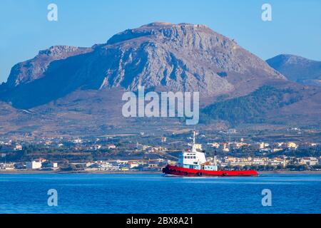 Journée d'été ensoleillée dans le golfe de Corinthe. Vue de l'eau au remorqueur en arrière-plan d'une petite ville sur une rive montagneuse Banque D'Images