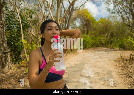 Portrait de style de vie extérieur de jeune femme asiatique attirante fatiguée et soif de boire de l'eau après la course dure séance d'entraînement au beau vert Banque D'Images