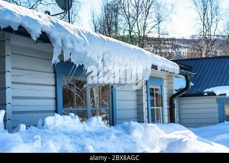 Photo de neige et de glaçons courbés suspendus du toit de la cabine suédoise traditionnelle en bois bleu clair dans les montagnes de Lapplet, dans le nord de la Suède. Banque D'Images