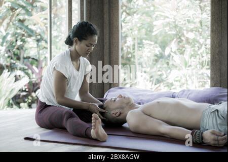 Jeune femme balinaise asiatique belle et exotique donnant un massage traditionnel de la tête et du visage thaïlandais à l'homme caucasien dans l'harmonie des soins de santé et Banque D'Images