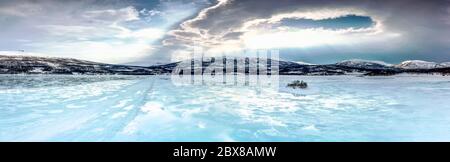 Panorama d'un lac gelé avec une petite île dans les montagnes du Nord qui commence à fondre, l'eau coule sur la surface de glace. Le ciel bleu et les rayons du soleil s'allument Banque D'Images