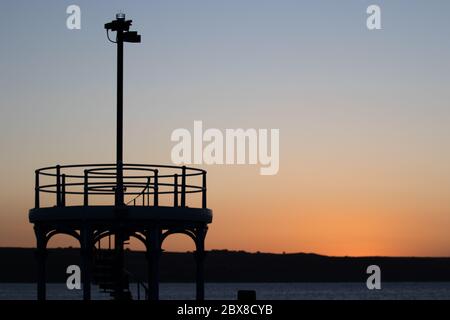 Weymouth, Royaume-Uni. 6 juin 2020. Le lever du soleil matinal silhouette la tour d'observation à l'extrémité de la jetée Stone Pier dans la baie de Weymouth. Banque D'Images