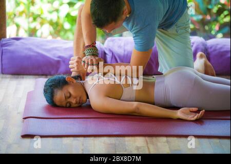 Jeune femme balinaise asiatique, belle et exotique, couchée sur un tapis de studio et recevant un massage thaï traditionnel par un masseur dans le jardin tropical du spa de bien-être Banque D'Images