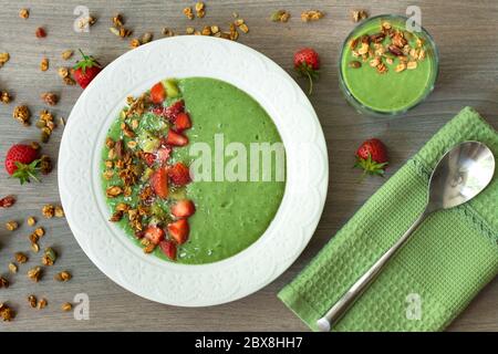 Bol à smoothie vert avec banane, fraise, épinards, chou vert, kiwi, lait de coco garni d'avoine maison, granola aux noix et graines, flocons de noix de coco, chia Banque D'Images