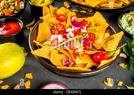 Croustilles nachos au fromage fondu et diverses sauces mexicaines traditionnelles, salsa et jalapeno, fond gris foncé vue du dessus espace copie Banque D'Images