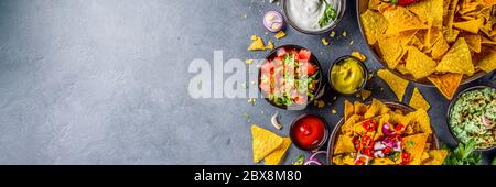 Croustilles nachos au fromage fondu et diverses sauces mexicaines traditionnelles, salsa et jalapeno, fond gris foncé vue du dessus espace copie Banque D'Images