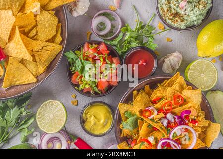 Croustilles nachos au fromage fondu et diverses sauces mexicaines traditionnelles, salsa et jalapeno, fond gris foncé vue du dessus espace copie Banque D'Images