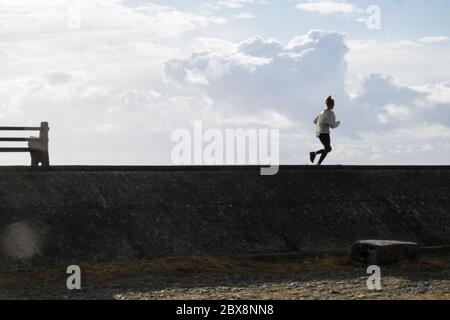 Littoral, local, femme, femme, silhouette, courir, courir, le long, promenade, dans, Borth. Prendre,elle,permis,exercice,quotidien,sur,une,journée,ensoleillée,sur,la,côte,côtière,littoral,vacances,station,village,de,Borth,nord,de,Aberystwyth,Ceredigion,Mid,West,Wales,Welsh,UK,GB,Britain,British,UK,.actuellement le pays de Galles est fermé aux touristes, pendant,Covid 19,coronavirus,calme,les paysages,non,les touristes,la pandémie,les touristes,les touristes,les touristes,les touristes,les touristes,les touristes, Banque D'Images