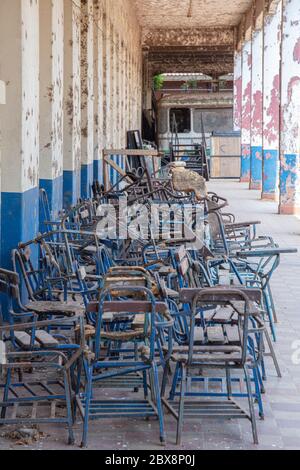 Une école secondaire abandonnée : vue le long d'un couloir extérieur de chaises poussiéreuses vers un bus scolaire abandonné, scène de la fin du monde Banque D'Images