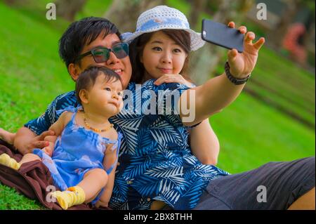 Jeune famille japonaise asiatique heureuse et aimante avec parents et petite fille douce au parc de la ville avec le père prenant le selfie pic avec téléphone portable Banque D'Images